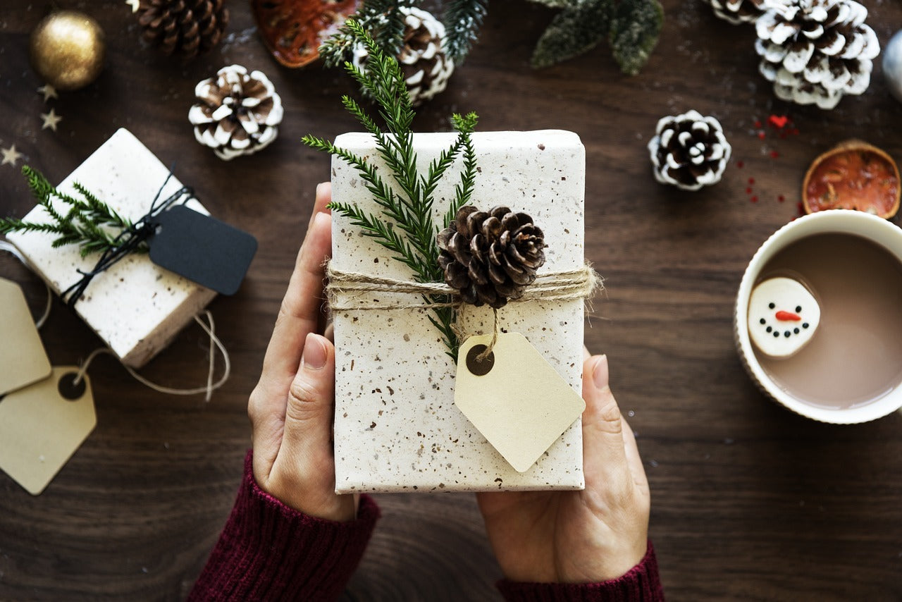 Person holding a gift box with decorative elements on a festive table setting.