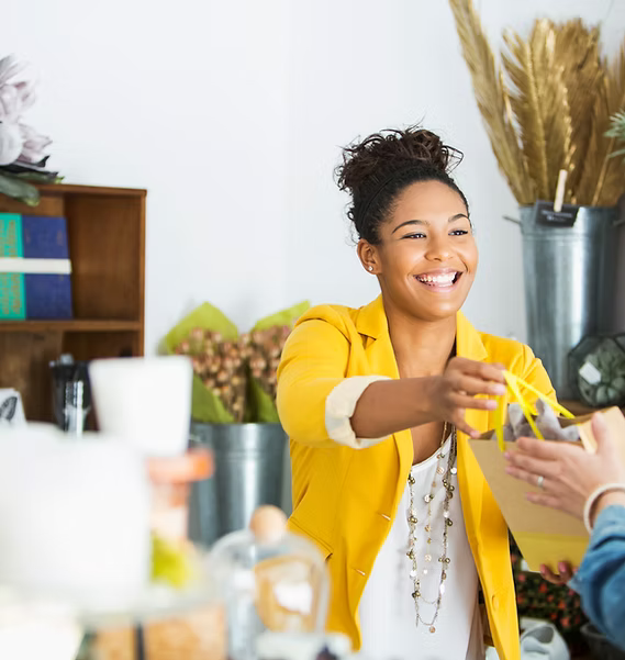 Woman in yellow jacket smiling and interacting with another person in a casual indoor setting.